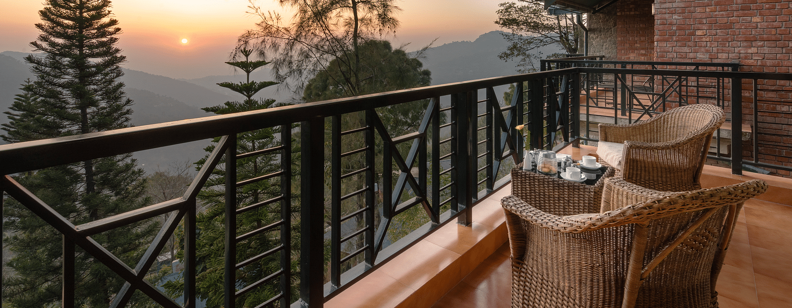 Two wooden chairs and a table set on an open balcony with a sunrise view -  Baikunth resort, kasauli 