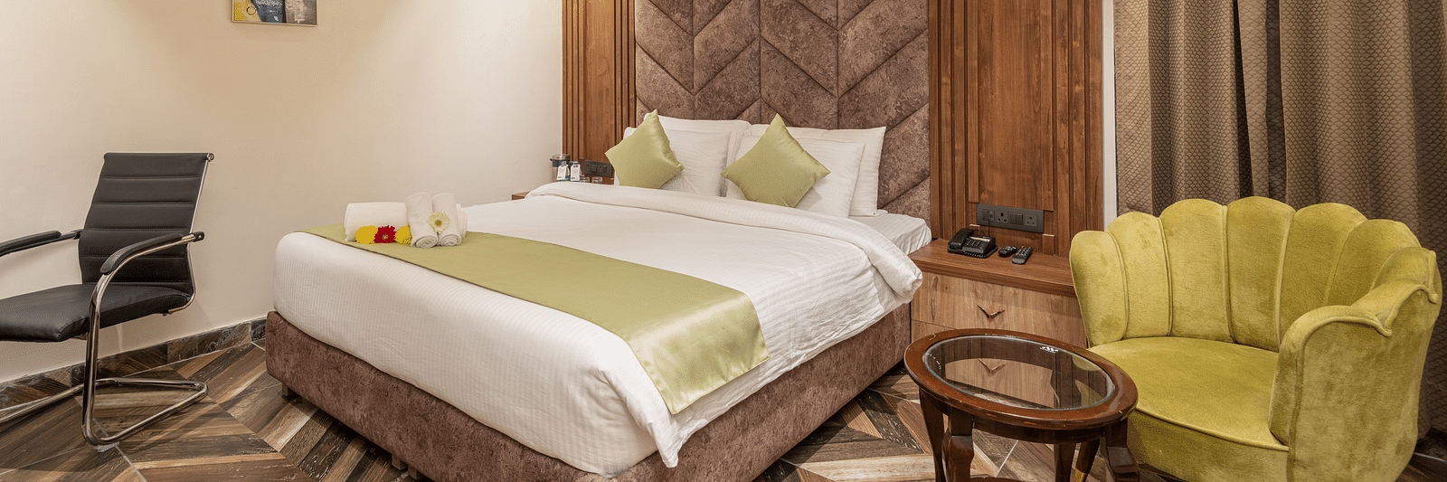 Image of Deluxe Room at DLS Grand Luxotica, Dehradun featuring a plush bed with a sitting space next to it by the window 