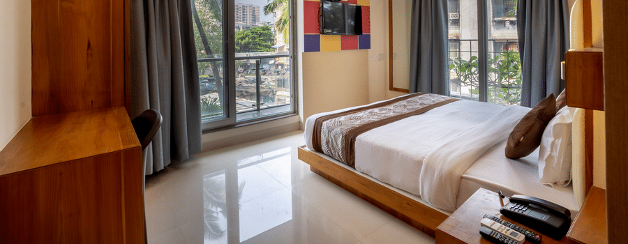 Home2 Suites & Service Apartments featuring a bed facing the TV on the wall with the door to balcony next to it, ready to be booked with exciting offers at Home2 India available on the official website