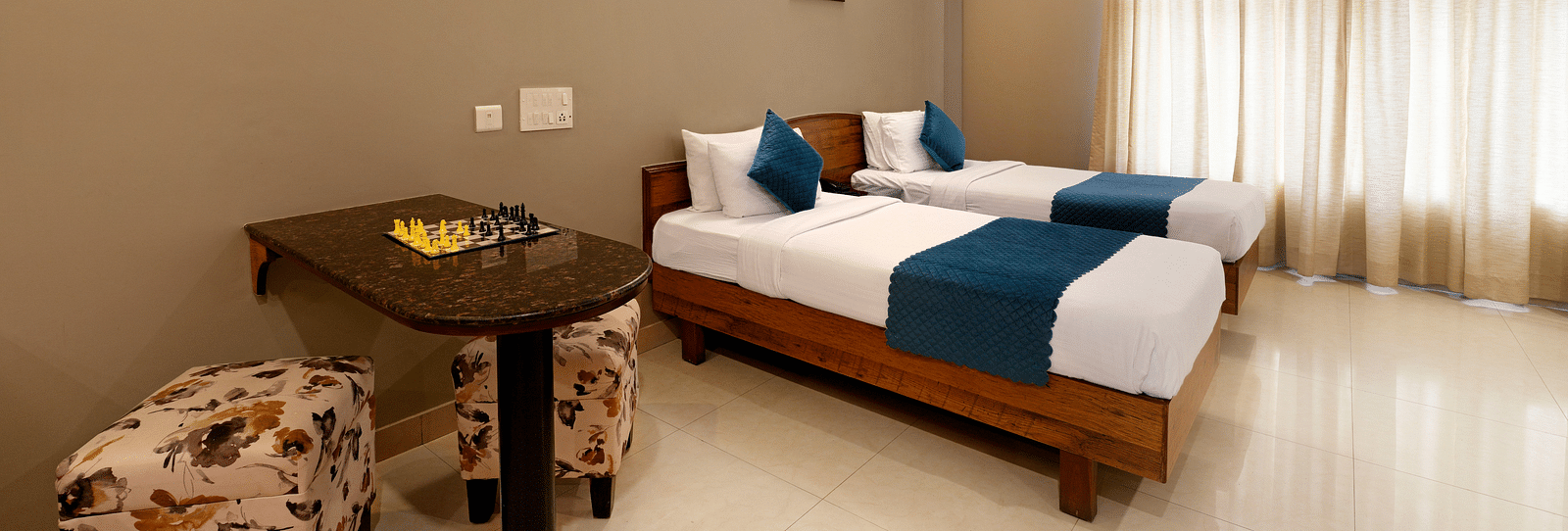 A Deluxe Room with a desk, twin beds, and bright natural light coming from the window - Cross Roads Inn, Bengaluru