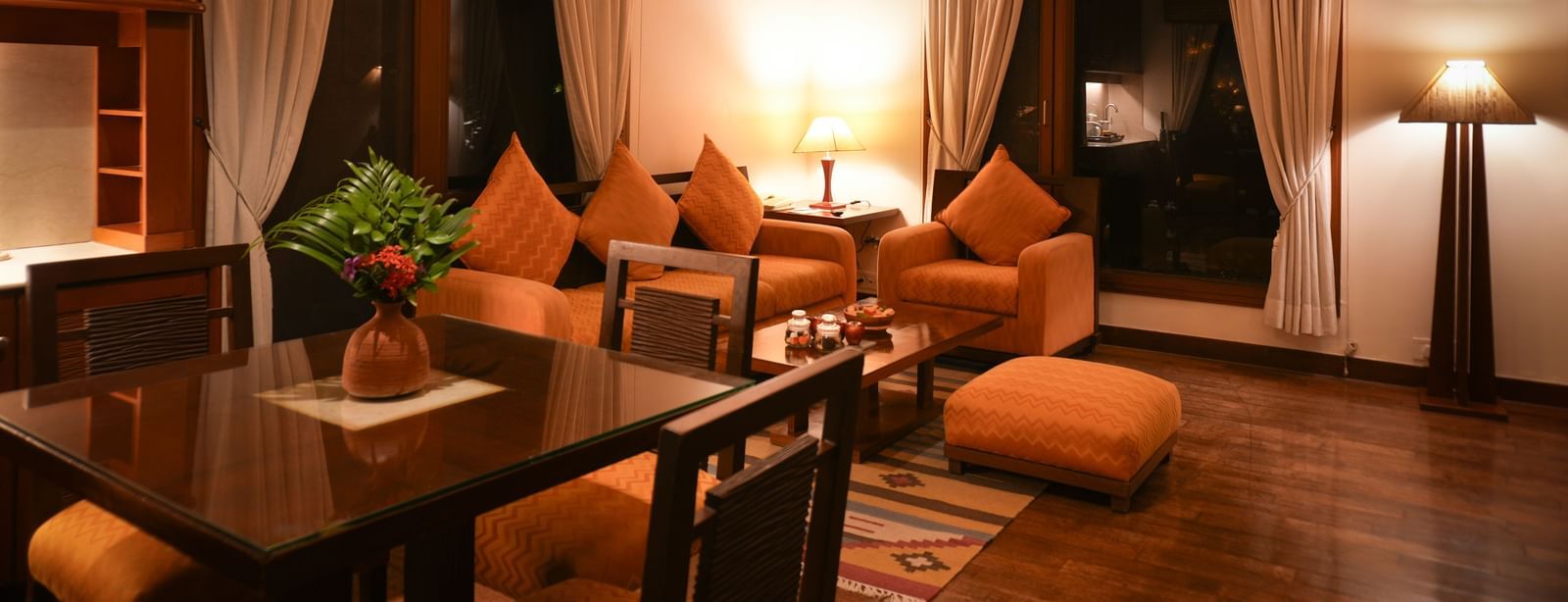 Different angle of the Lake View Villa’s living area at Vedic Village Spa Resort showing wooden flooring, earth-toned couches, and an in-room dining table.