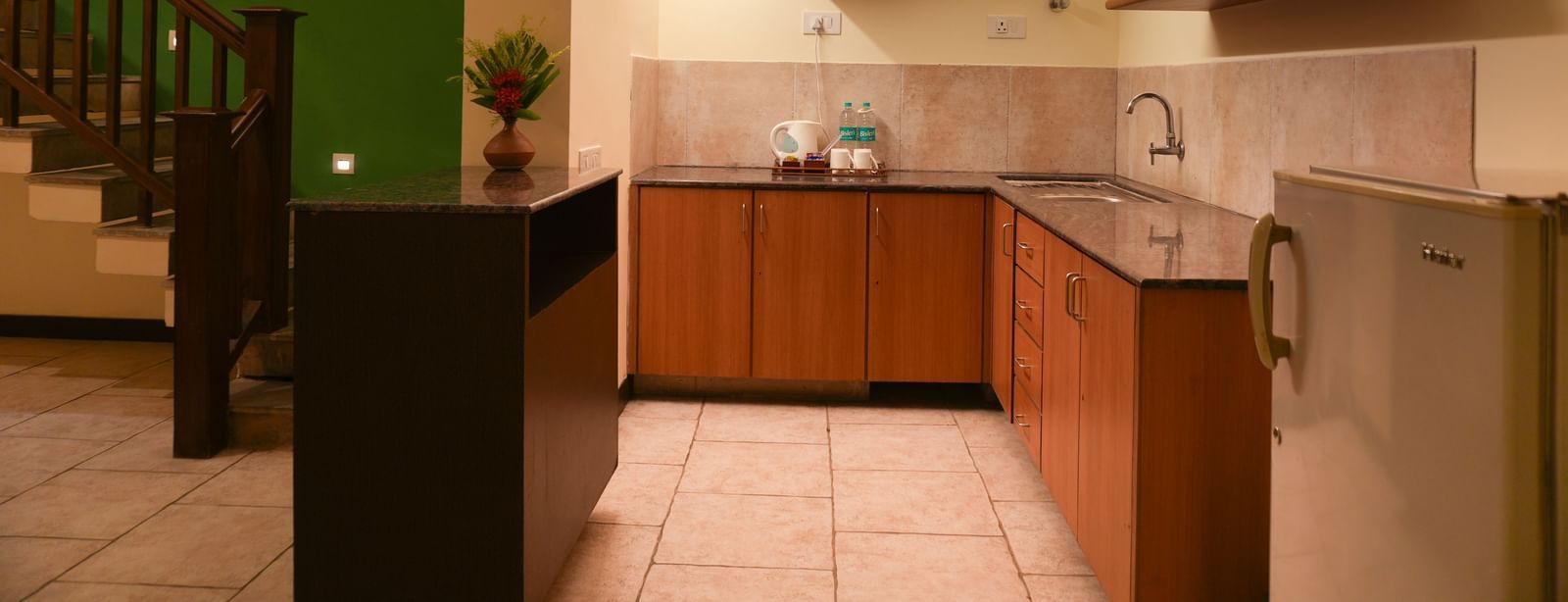 Compact kitchen in the Retreat Villa at Vedic Village Spa Resort with a mini fridge, wooden cabinets, sink area, and an electric kettle.
