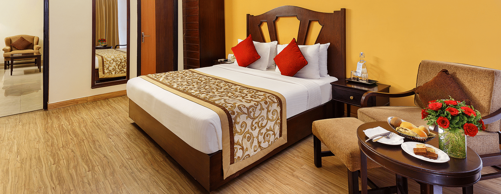A side angle image of the room featuring a king size bed, coffee table and a wall painting hanging on the wall an d a TV.