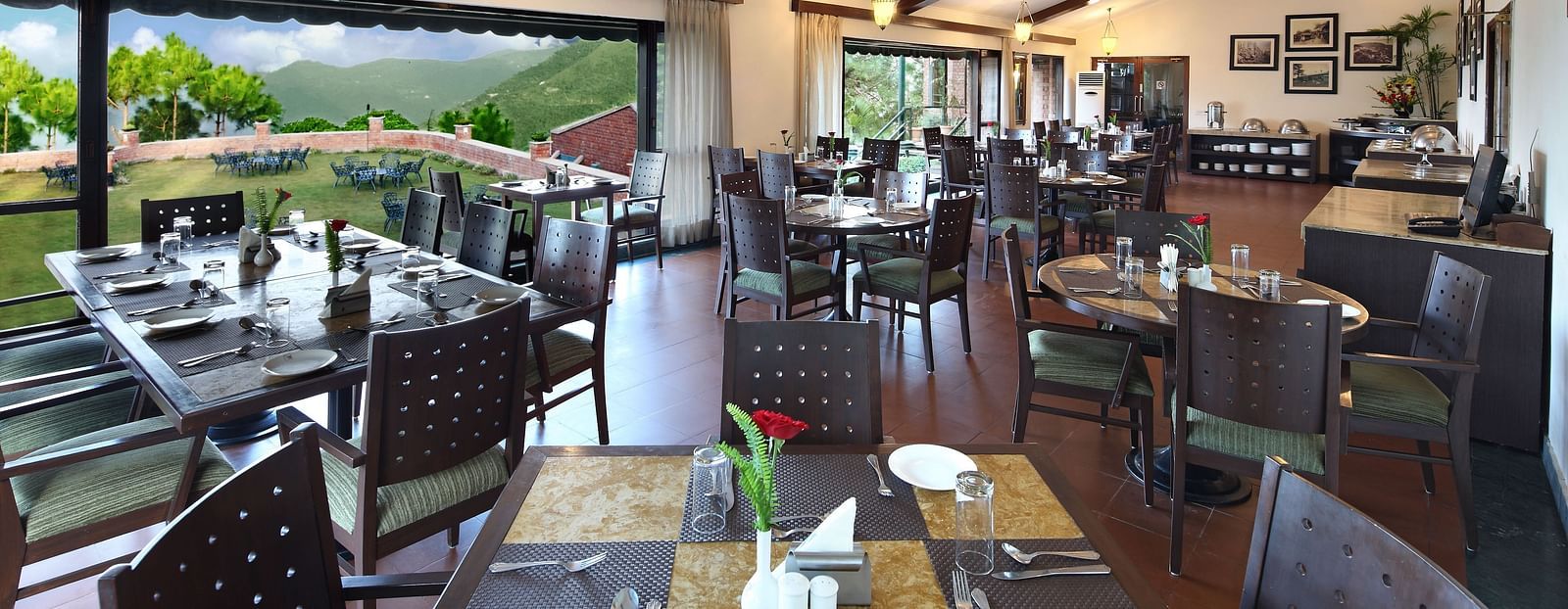 An image of a Restaurant area with wooden chairs and tables which has plates and cutlery on top At baikunth Resort, Kasauli