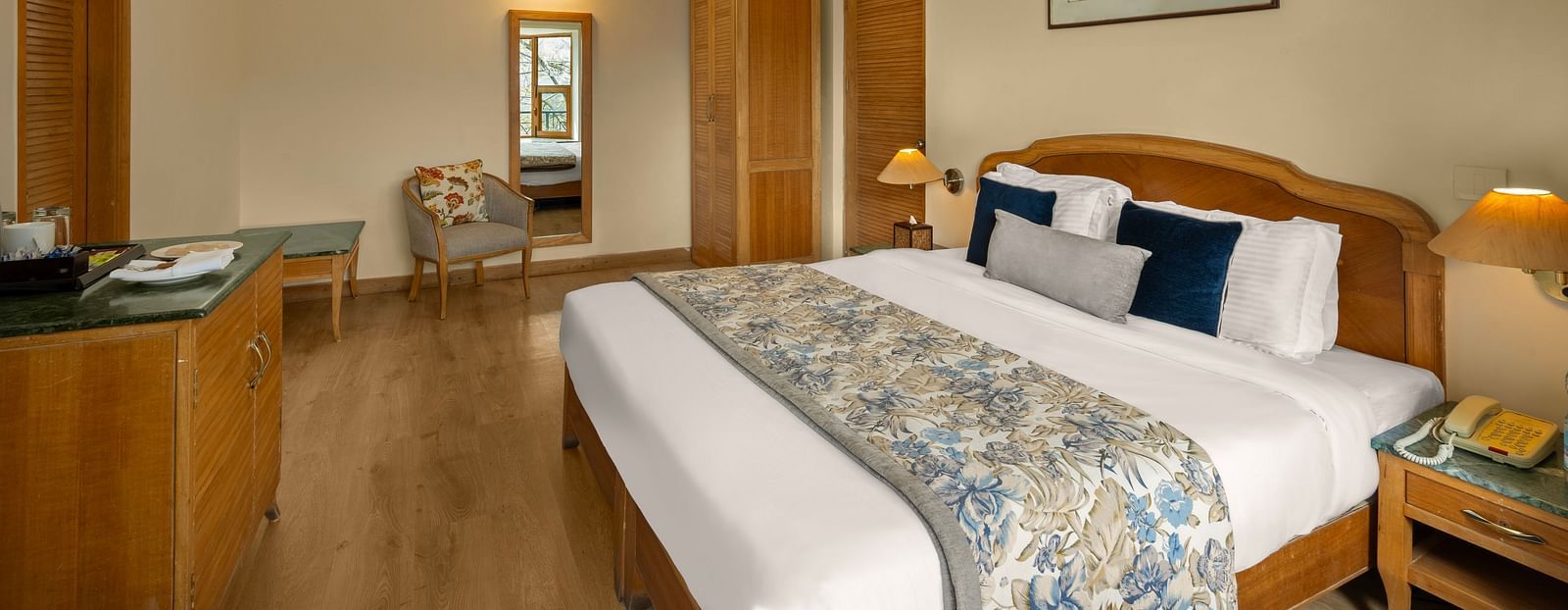 A side view of Superior Cottage Hill View bedroom showcasing a double bed, a side table, and a wardrobe with a mirror adjacent to it -  Baikunth resort, kasauli 