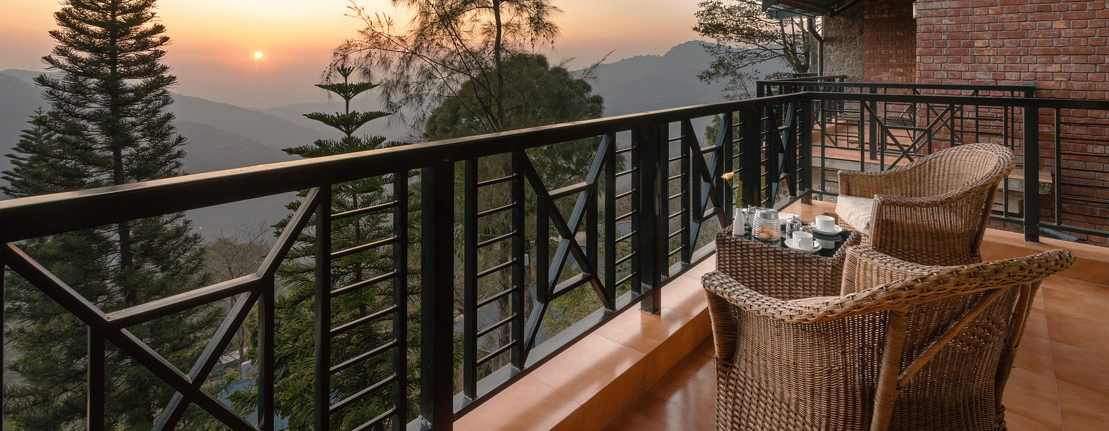 Two wooden chairs and a table set on an open balcony with a sunrise view - Baikunth resort, kasauli 