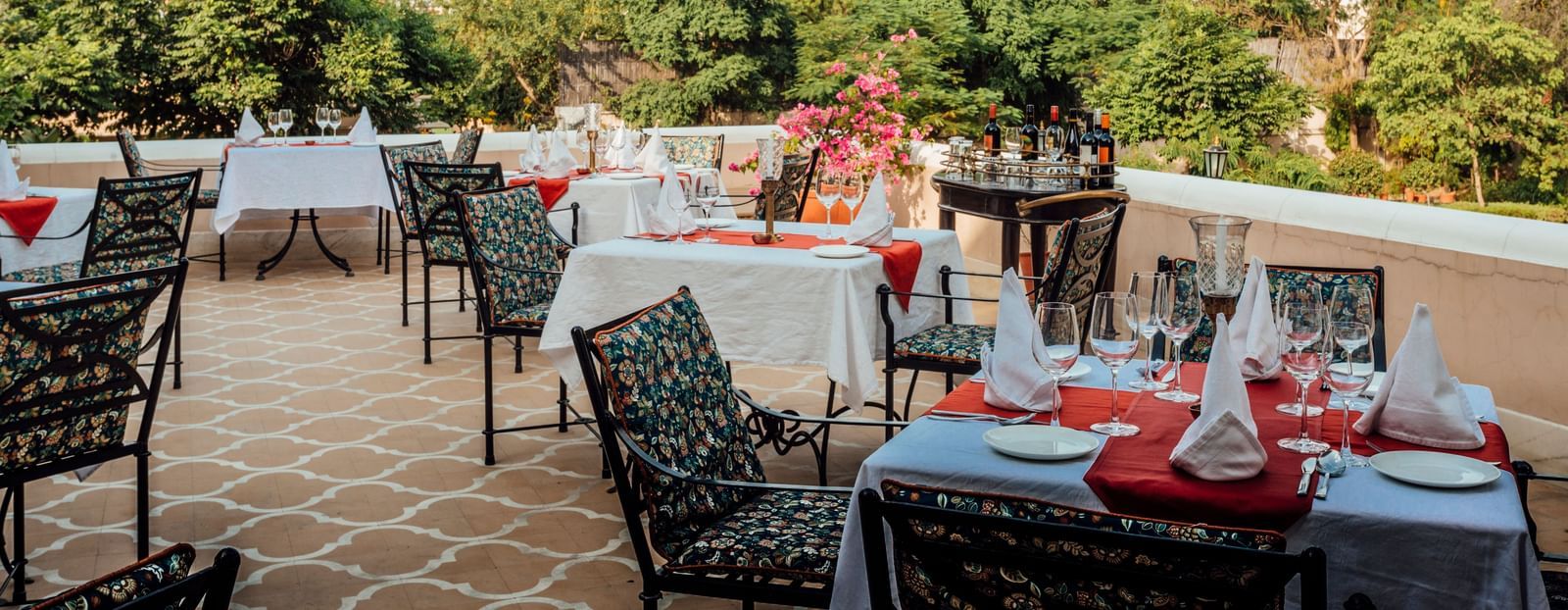 An outdoor dining terrace at Royal Heritage Haveli with tables set, overlooking trees and a distant landscape.