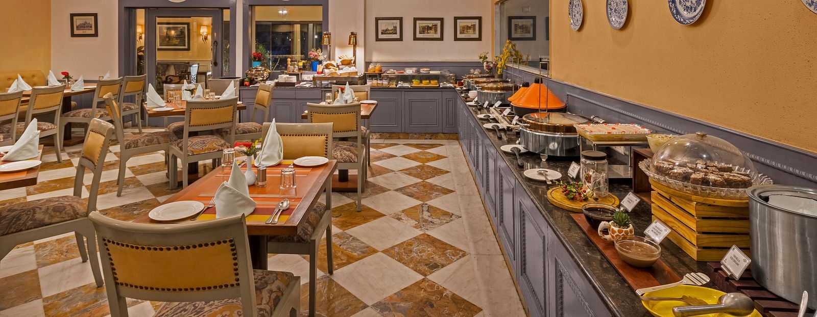 an image of a restaurant with a buffet setting and clusters of tables with chairs - The Manor, Kashipur