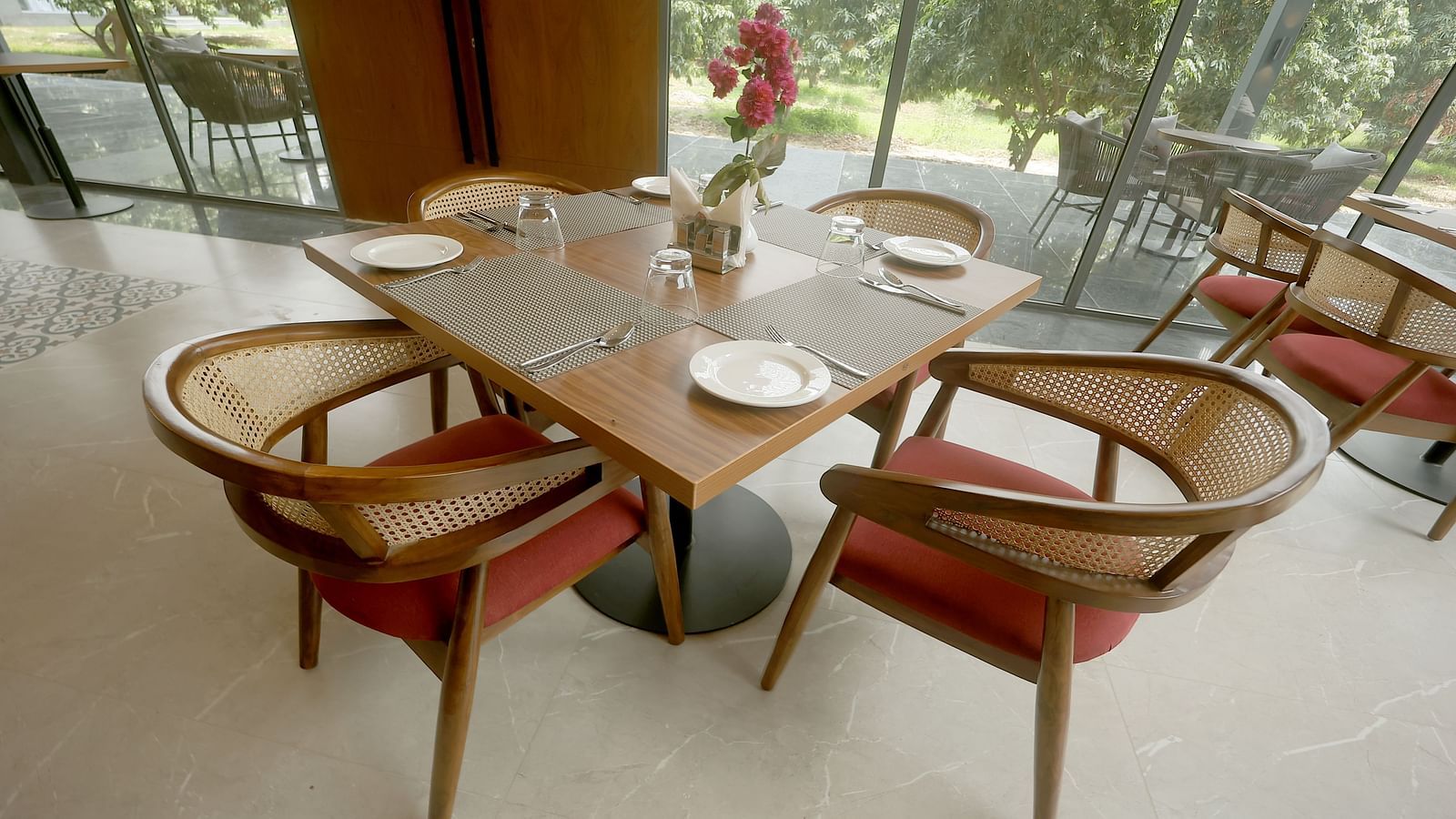 Bright restaurant seating arrangement with wooden chairs and a view of greenery through full-height windows at Wyndham Garden.