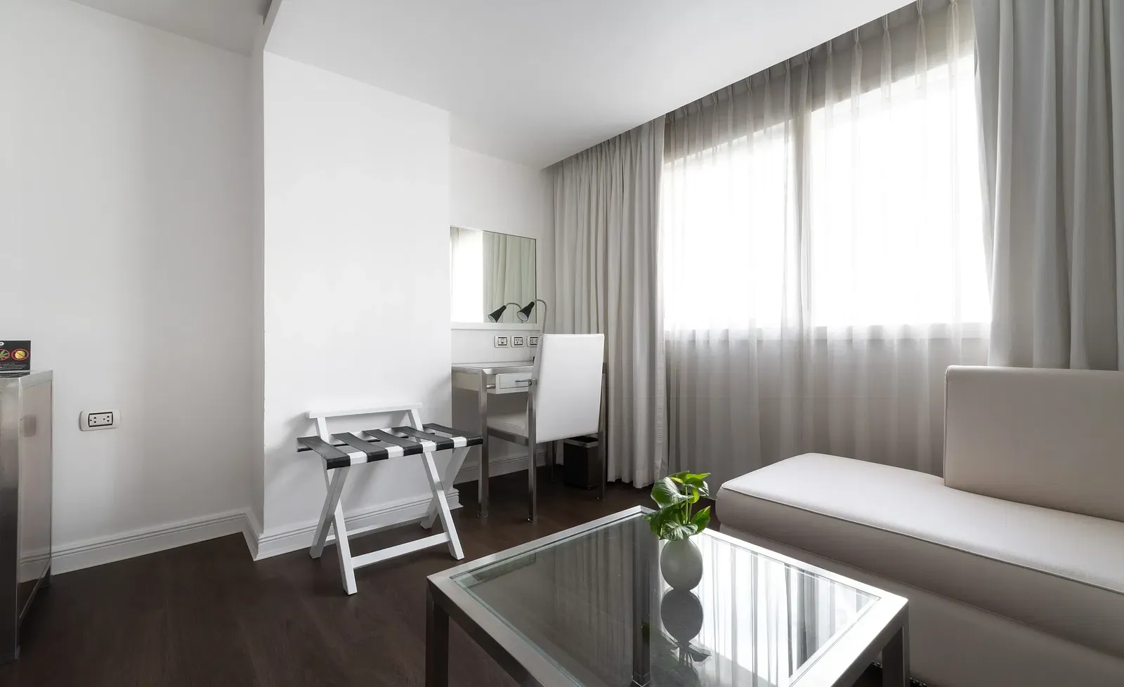 Minimalist hotel workspace with white desk, black checkered chair, cream sofa, glass table, and neutral decor creating a sophisticated ambience at Night Hotel Bangkok.