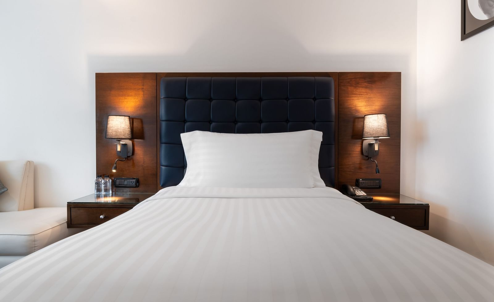 King bedroom with tufted headboard, dark wood floors, and modern chair at Night Hotel Bangkok.