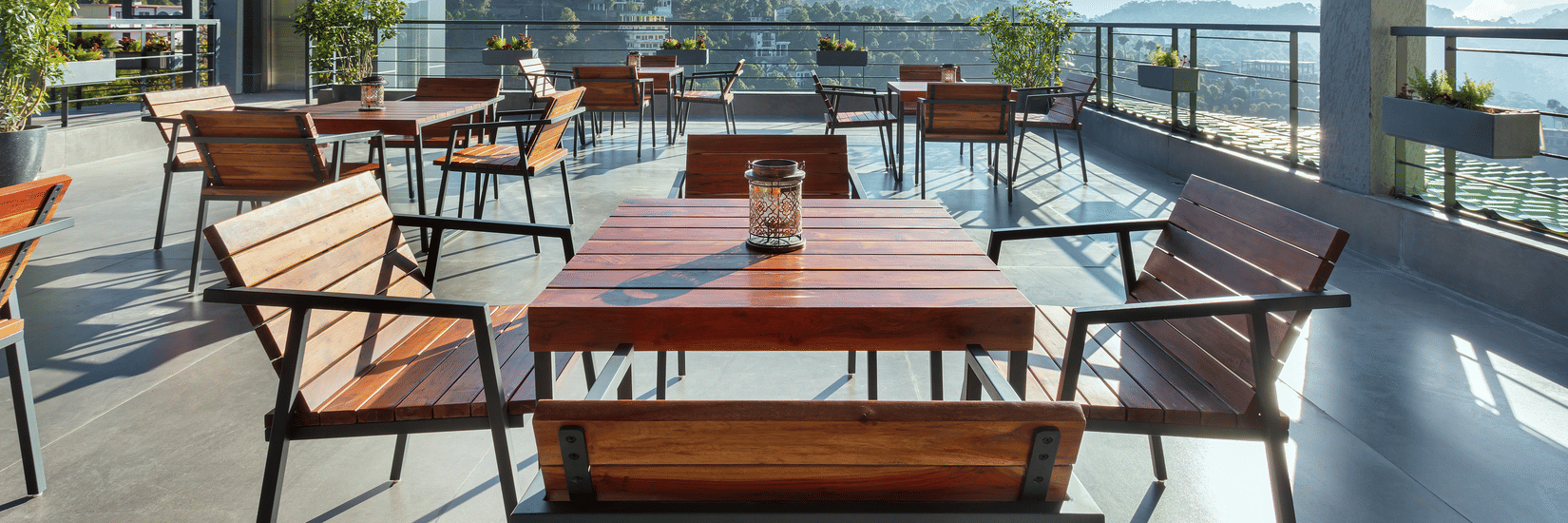 Outdoor dining area at Suryavilas Luxury Resort and Spa, featuring wooden tables and chairs on a spacious terrace with panoramic views of the Himalayan hills under a bright blue sky.