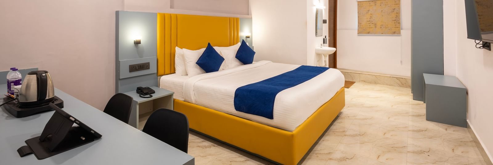 Full view of a modern Premium Room with a bed featuring blue accents, a work desk area, and a door on the left  - Beestay Hotels Financial District, Hyderabad 