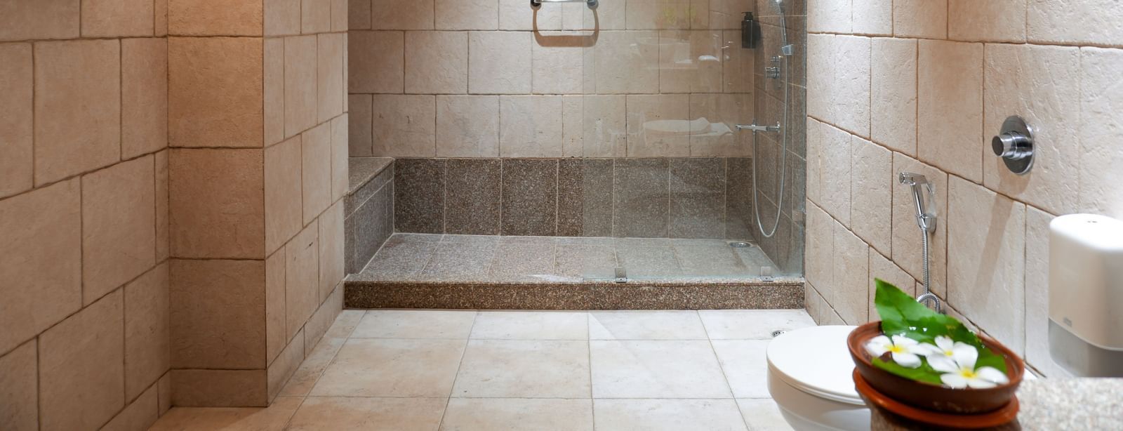 Well-lit washroom in the Retreat Villa at Vedic Village Spa Resort featuring ambient lighting, a transparent glass shower cubicle and a western commode.