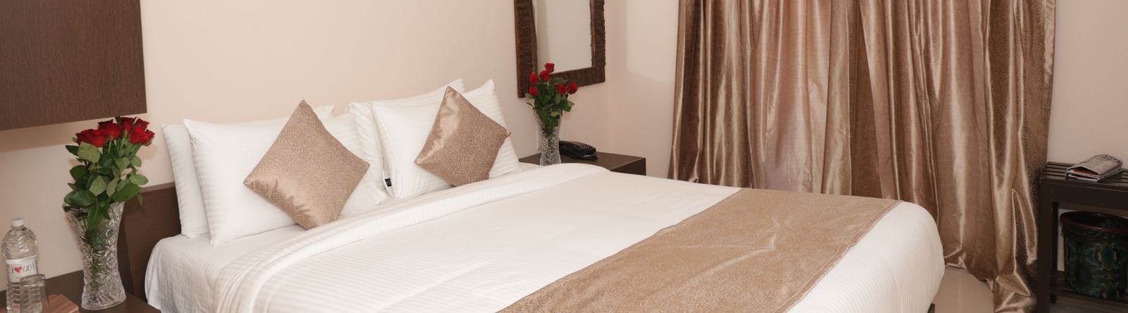 A bed with bedside tables, flowers, wall art, a mirror and window curtains at Nazri The Verda Hotel, Arambol.