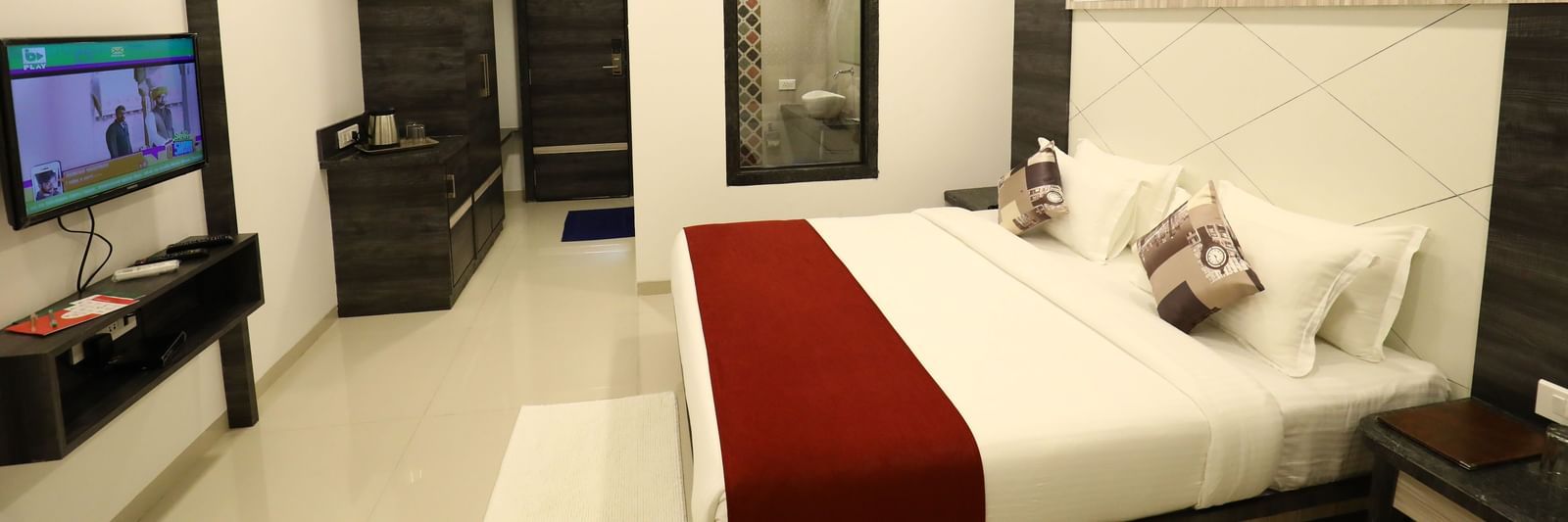 A room in Imperial Grande with a bed covered in white and red bedding, a television on a stand, and a mirror on the wall.