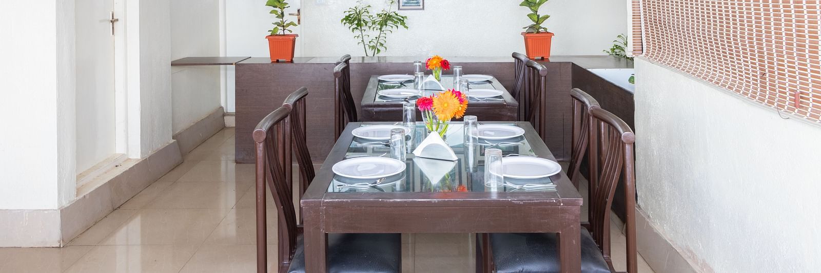 A dining area with a wooden table, chairs, and decorated with framed pictures and potted plants at Sanctum Suites Domlur, Bangalore.