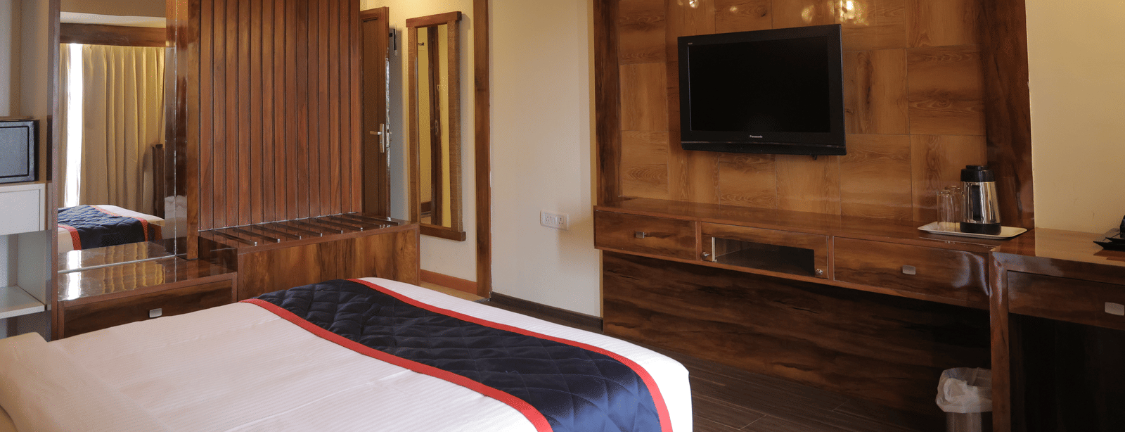 A cosy hotel room featuring a large bed, wooden furnishings, and a wall-mounted television - Benzz Park, Kodaikanal