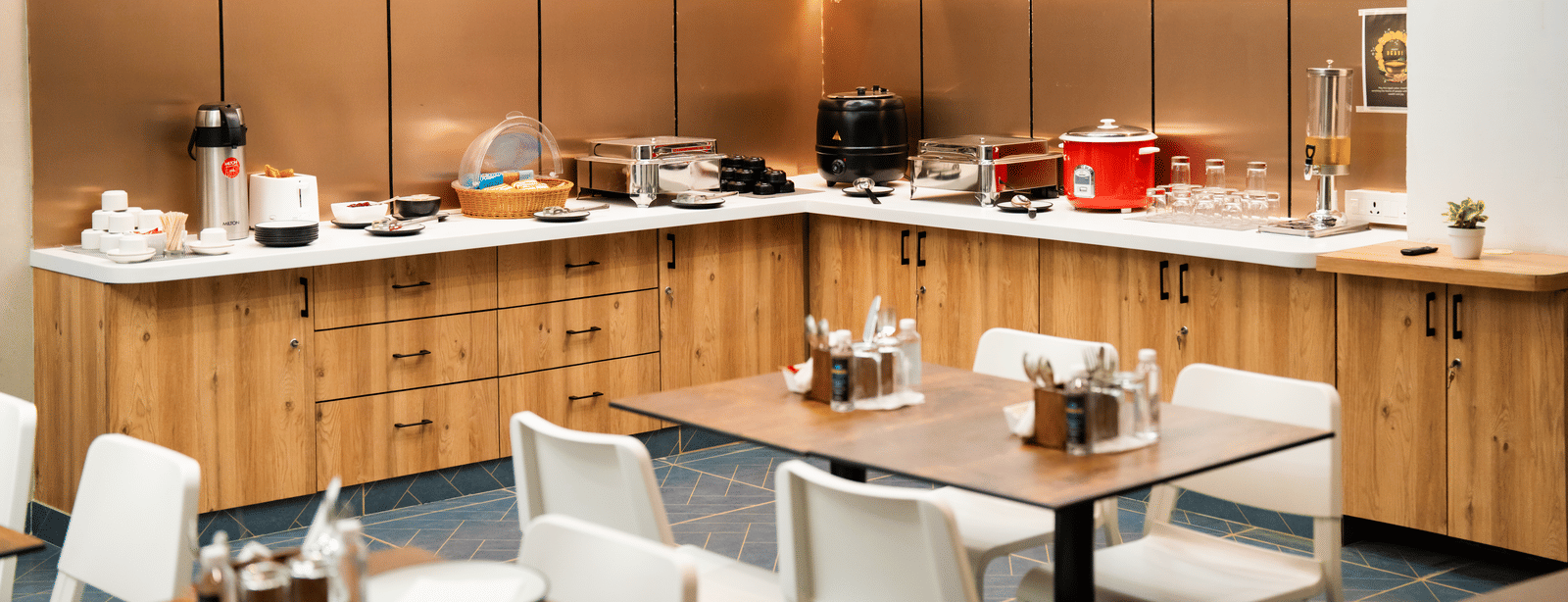Buffet area with various dishes displayed, and tables with chairs neatly arranged in front at Sunrise Business Hotel, Hyderabad.