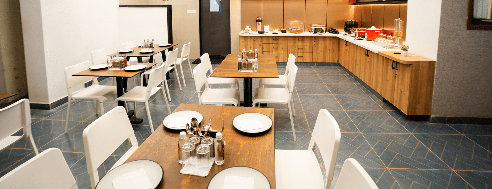 View of the restaurant with dining tables and chairs set, and a buffet counter in the background at Sunrise Business Hotel, Hyderabad.