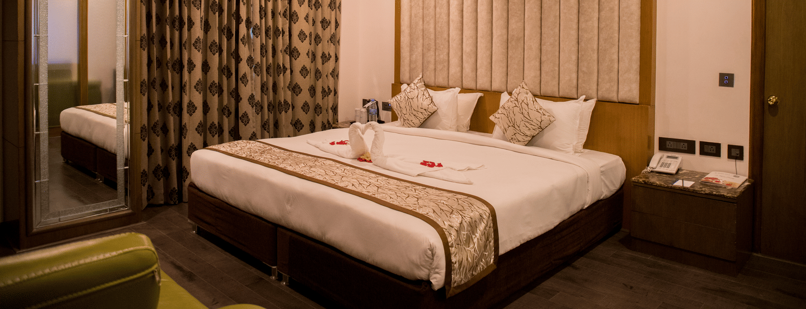 A hotel room at Benzz Park Chennai featuring a neatly made bed with white linens, a bedside table, and curtains.