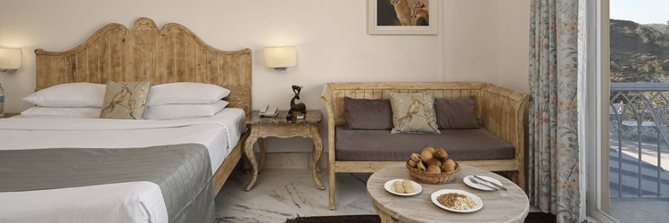 Superior Room with Balcony at Fateh Safari Resort, Kumbhalgarh featuring a double size bed, bedside tables with lamps on either side, a sofa with centre table, and an attached balcony.