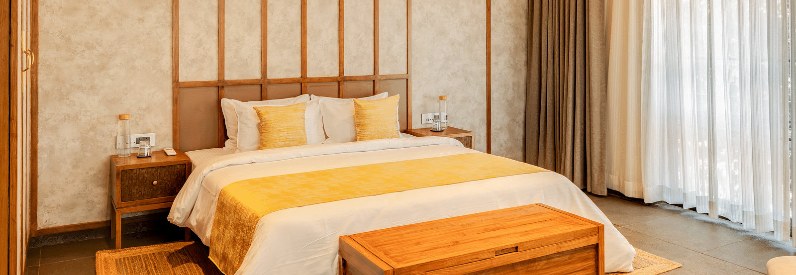 A cosy bedroom with a king-sized bed, yellow accents, and warm wooden panelled walls, enhanced by natural light from large windows - BluSalzz Villas - Alocassia, Anjuna