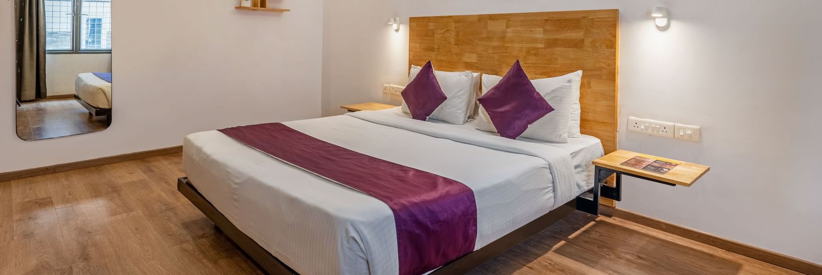 A hotel room with a double bed, wooden flooring, a large mirror and a side table - Monday Hotels HITEC City, Hyderabad