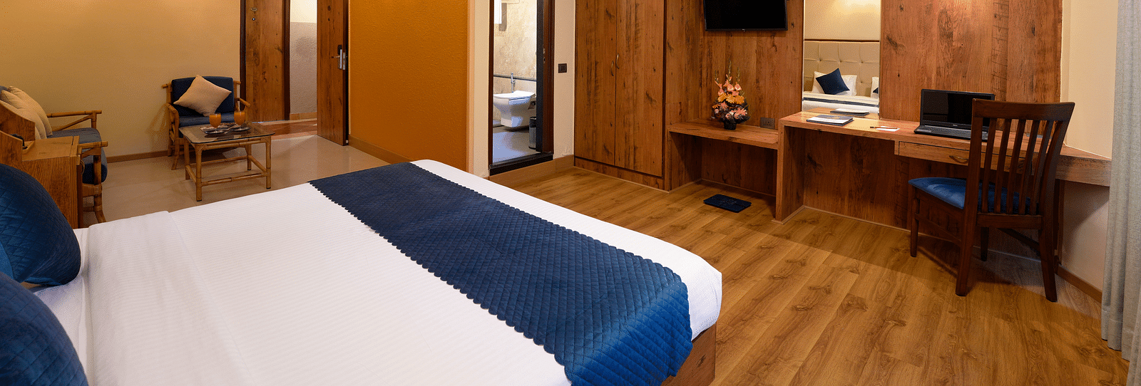 A well-furnished hotel room with a queen size bed, a seating area and wooden furniture - Cross Roads Inn, Bengaluru