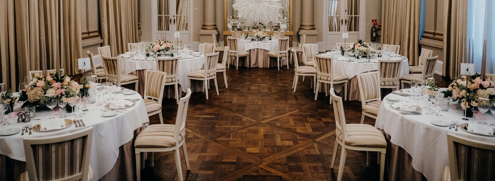 A grand ballroom featuring multiple round tables with linens and warm lighting