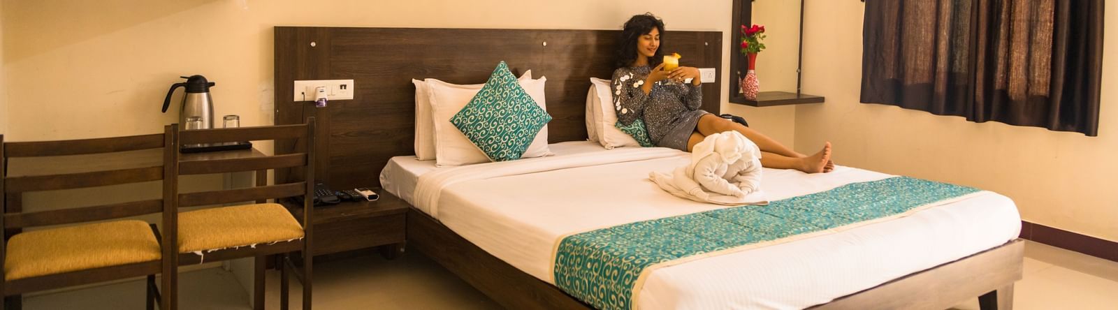 A guest room with a double bed, chairs, and dressing area, with a woman seated at Daksh Resort & Amusement Park.