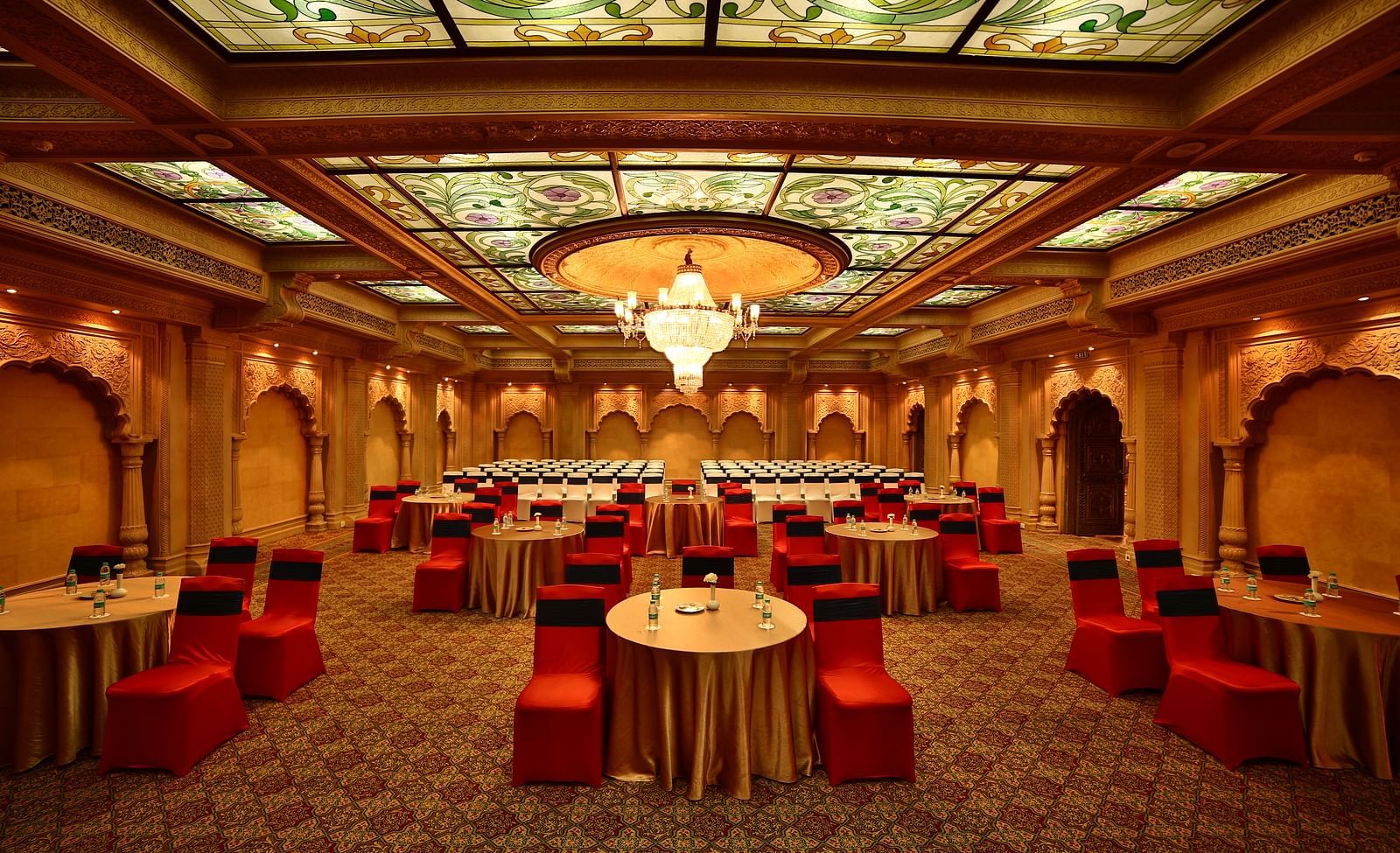 Seating arrangement in Taj Mahal Hall A grand hotel suite with an opulent red and white decor, large bed, and seating area, reflecting a traditional style at Sitara Luxury Hotel in Hyderabad near Ramoji Film City.