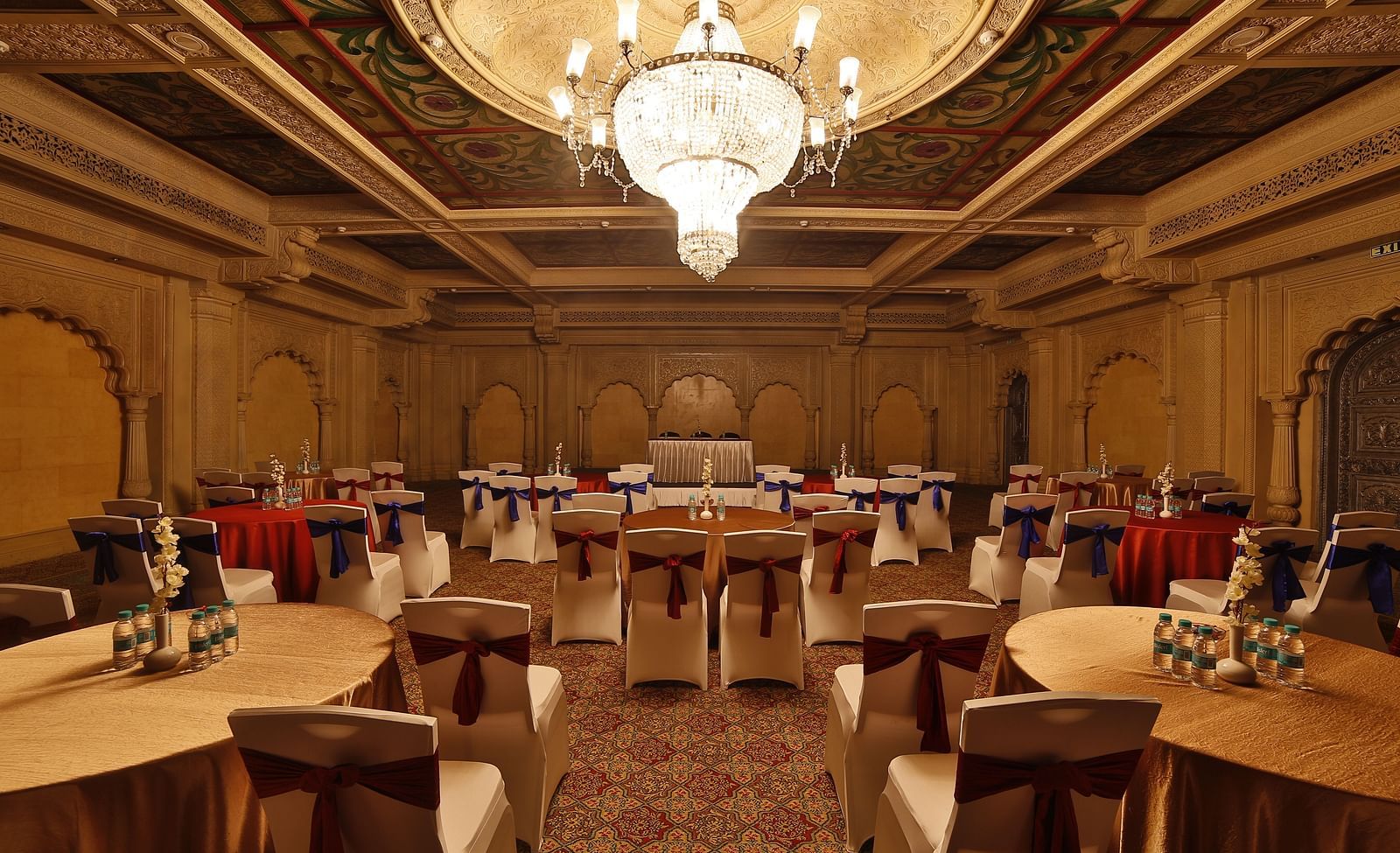 Seating arrangement in Taj Mahal Hall A grand hotel suite with an opulent red and white decor, large bed, and seating area, reflecting a traditional style at Sitara Luxury Hotel in Hyderabad near Ramoji Film City.