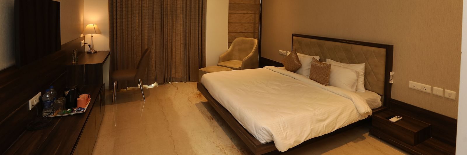 Hotel bedroom interiors with chairs television and a white king size bed - Welcome Inn Hotels