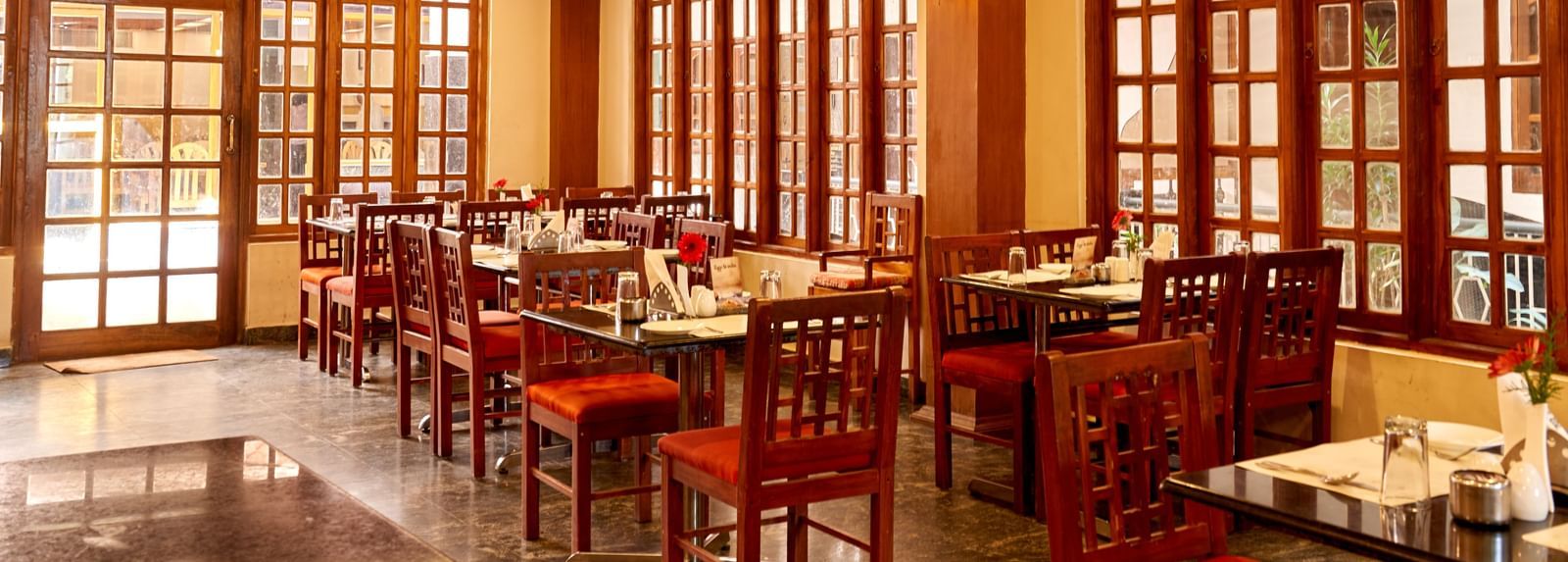 Log shot of the inviting dining area at Hotel Mamallaa Heritage, with red chairs, wooden tables, and natural light filtering through large windows.
