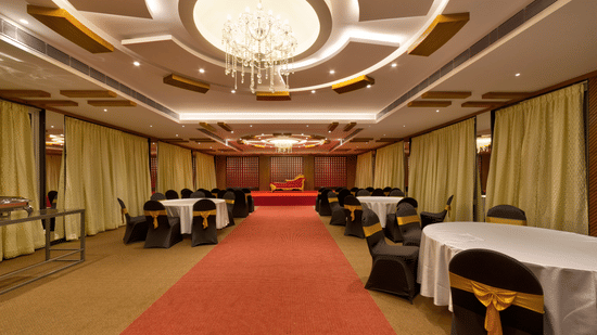 A red carpet, a decorative chandelier, and round tables with white cloths in the banquet hall at Icon Express By Bhagini, Mahadevapura.