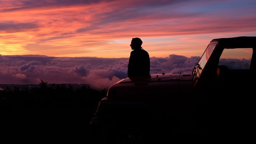 a person sitting on the hood of a car looking at the different hues in the sky