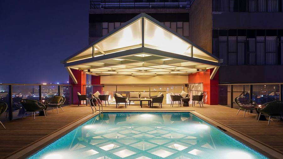 An image of a Skydip Pool Deck Bar featuring sets of tables and chair around a swimming pool at The Orchid Hotel Chandigarh