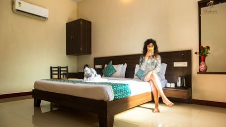 A woman sitting on a bed in a guest room featuring wooden furnishings and an air-conditioning at Daksh Resort & Amusement Park.