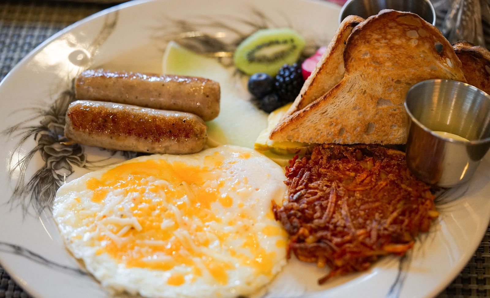 A full breakfast spread featuring sunny-side-up eggs, sausage, crispy hash browns, and a slice of toast - Brewery Gulch Inn & Spa