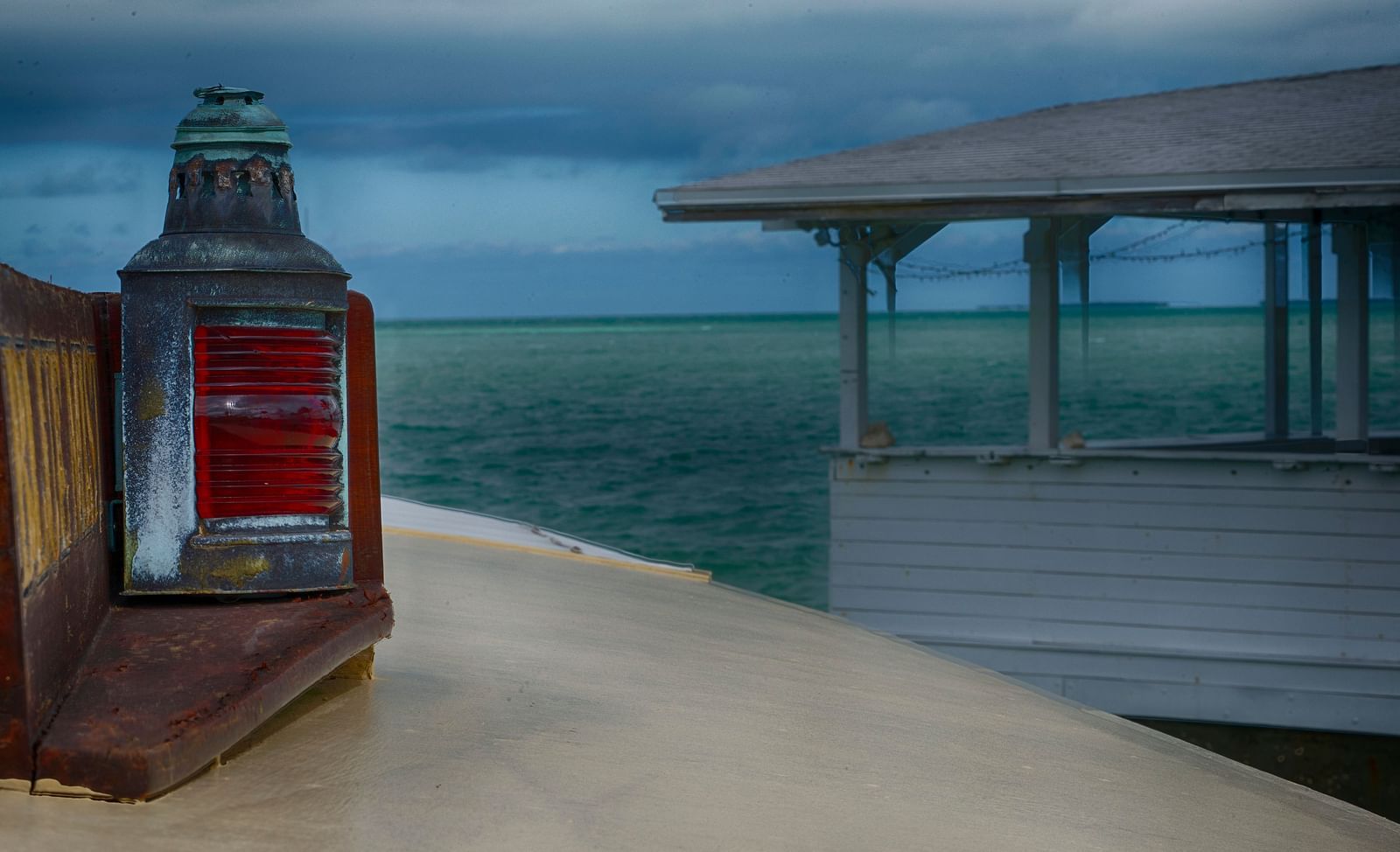 A red lantern on a wooden walkway at Casa Morada, with a white overwater structure and ocean view in the background.