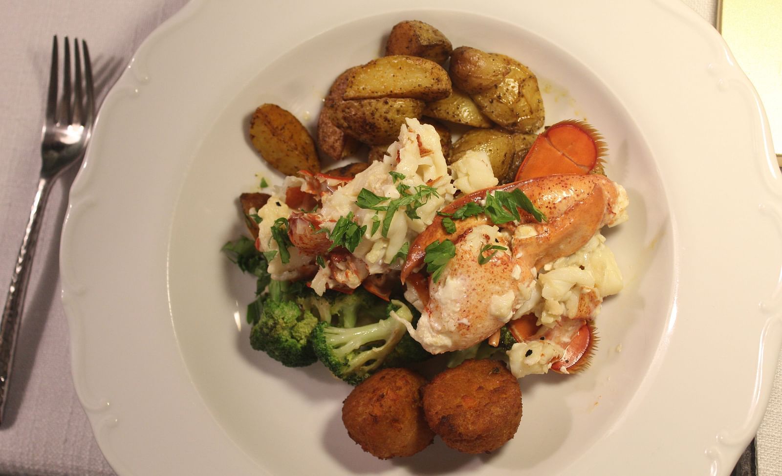 Lobster served with potatoes, greens, and vegetables on a white plate.