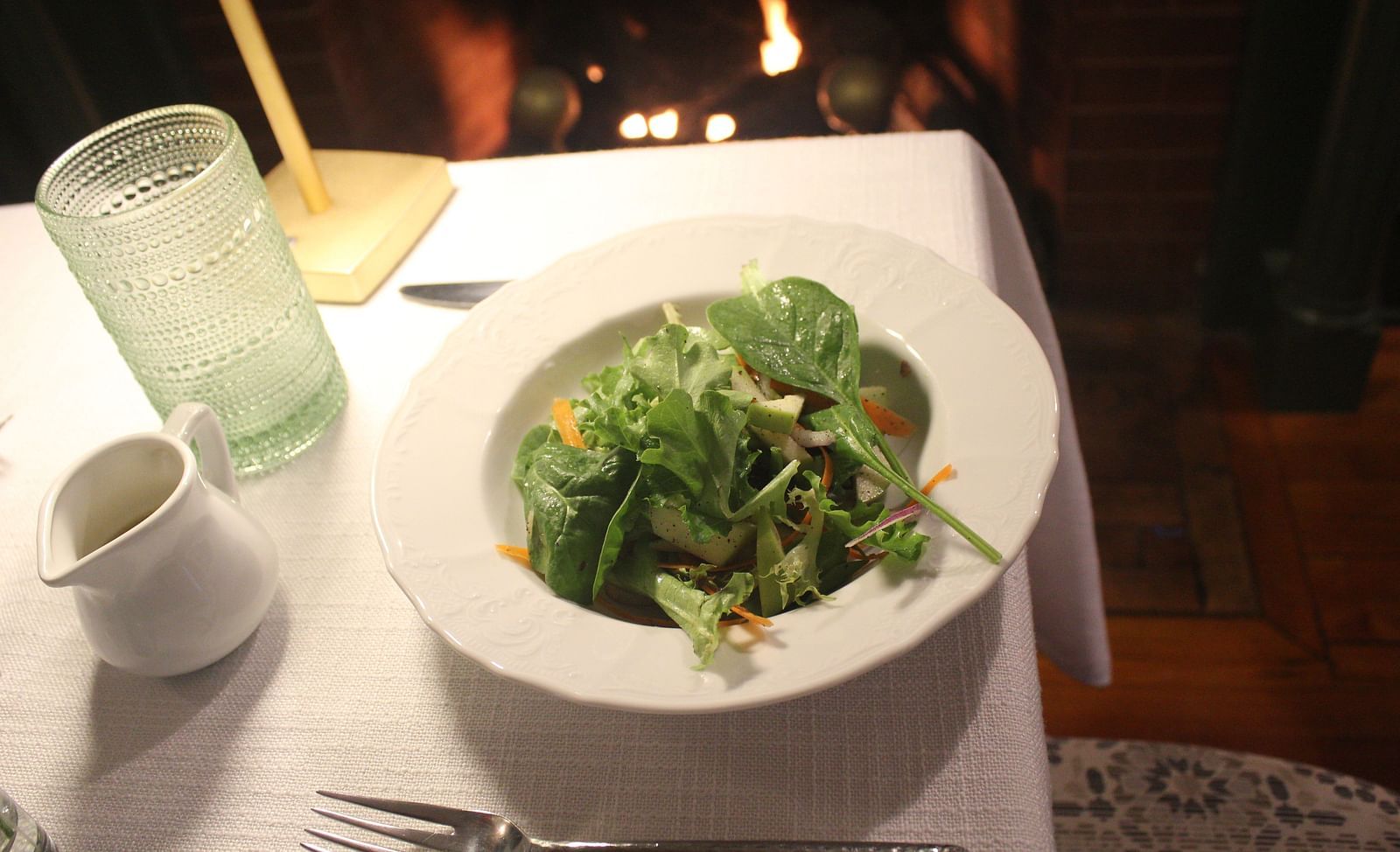 A plated green salad on a white tablecloth beside a water glass.