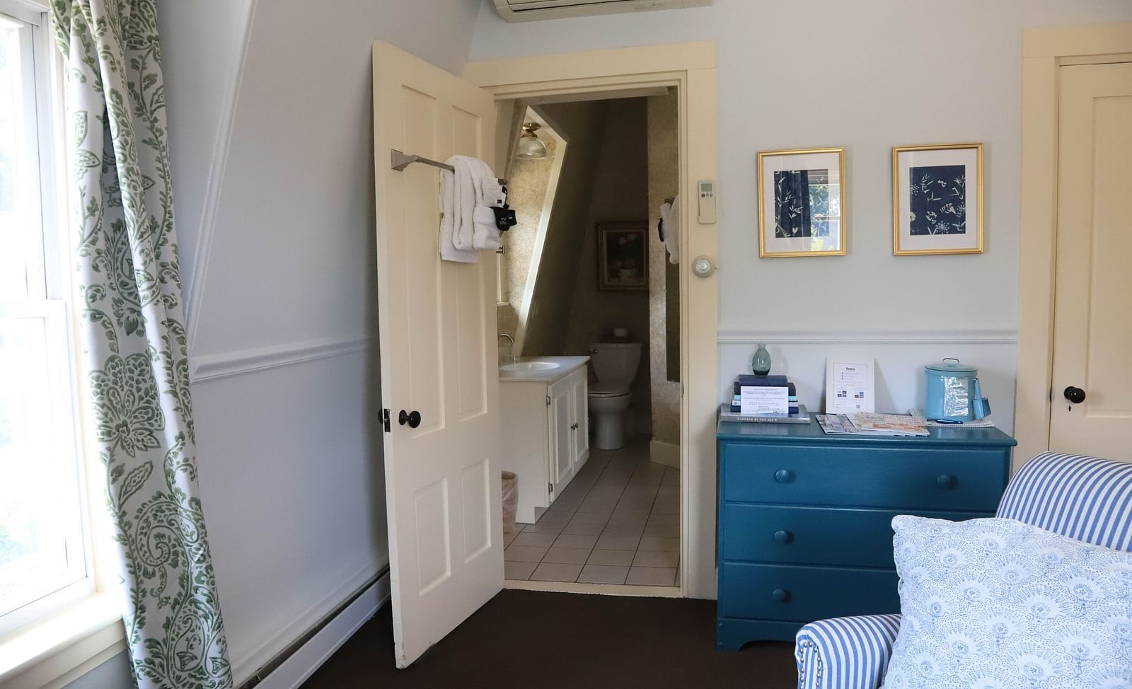 Cozy room with blue table and showing the bathroom from far with vanity sink and towel hanging  at Hartstone Inn.