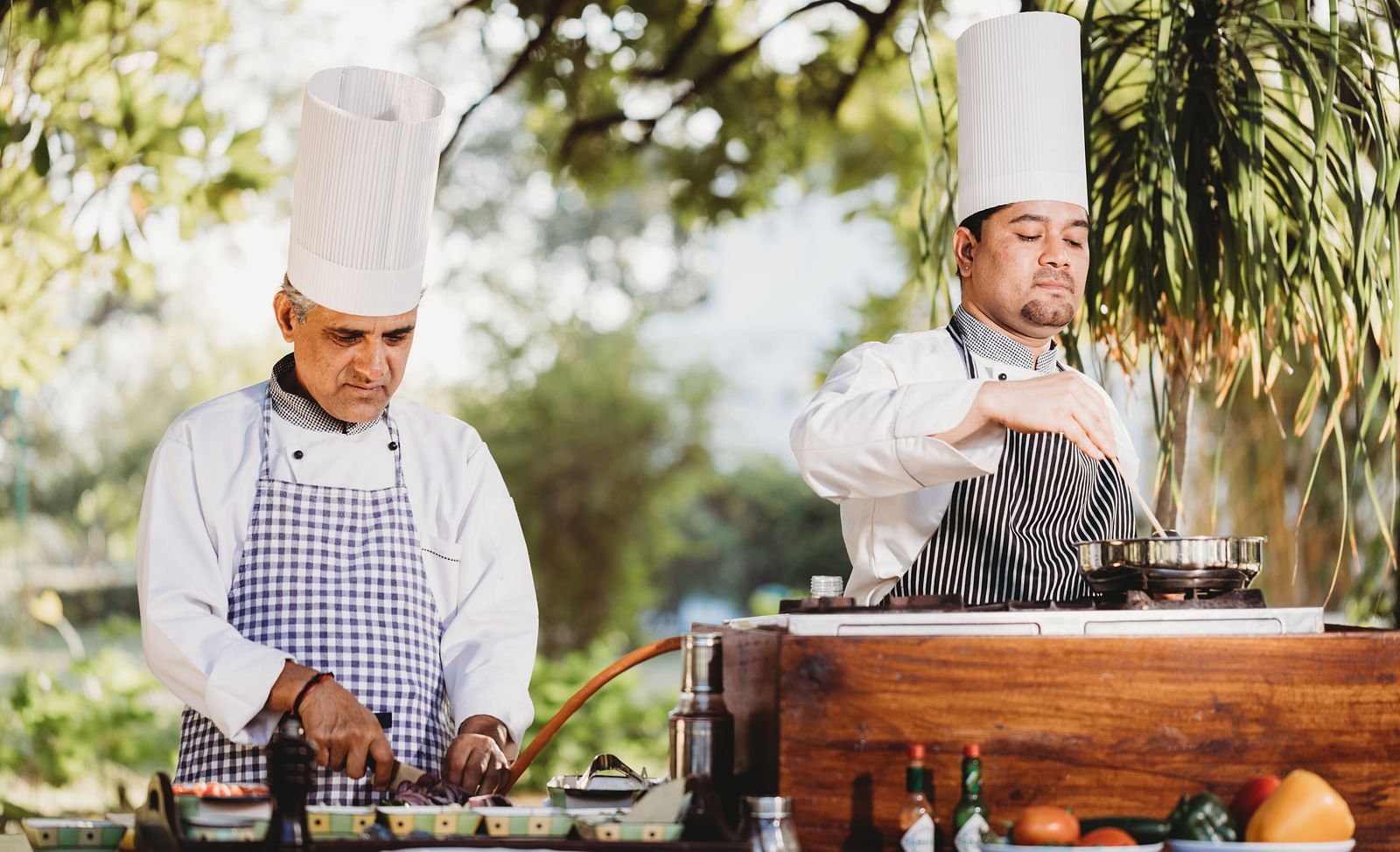Two men with chef's hat cooking with a big stove in front of them- Shahpura Bagh.
