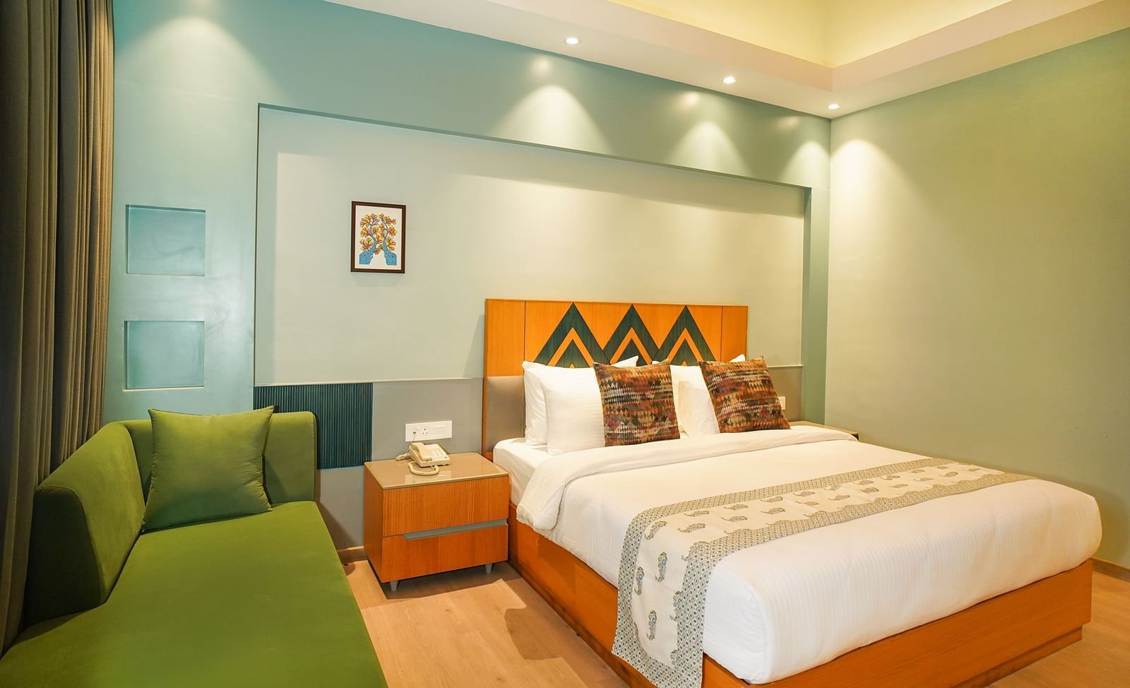 A hotel room showcases a neatly made bed with a green throw blanket, a bedside table with a lamp, and a green sofa | Deluxe Room with Valley View | Sukama Resort & Spa, Nainital
