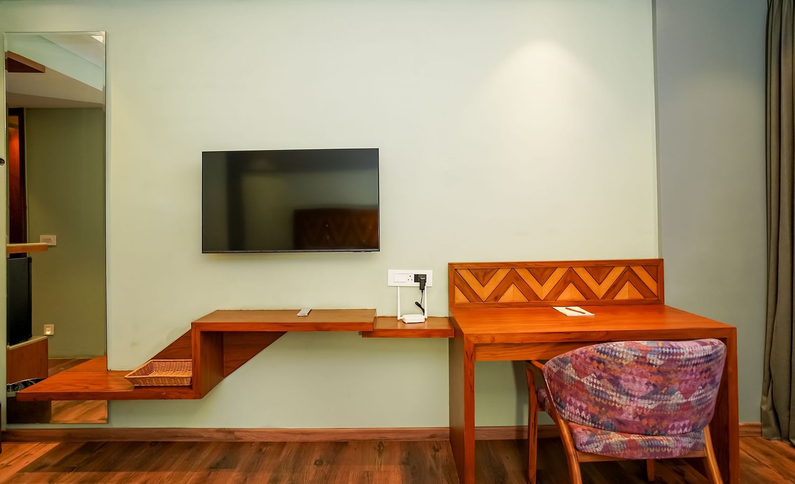 A hotel room's desk area showcases a wall-mounted television above a wooden desk with a red upholstered chair | Deluxe Room with Himalayan View | Sukama Resort & Spa, Nainital