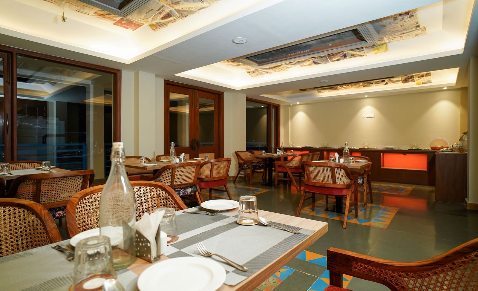 A dining table set with plates and cutlery in a restaurant setting with warm lighting | Sukama Resort & Spa, Nainital