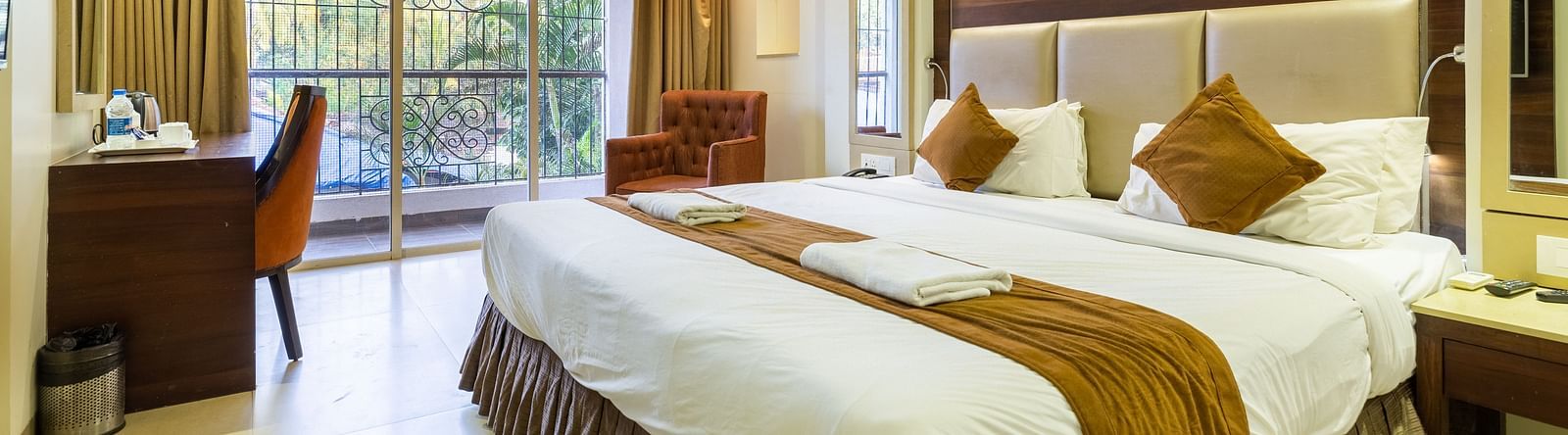 Image of a room with a bed and a table with a chair in the corner at Calux Grand Inn, Calangute.