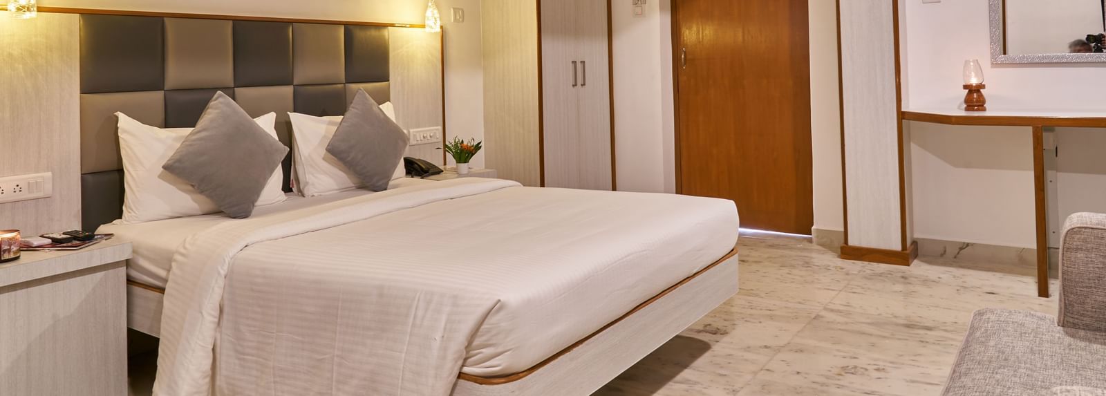 A bright and inviting hotel room at Hotel Mamallaa Heritage, featuring a bed with white linens, a bedside table, and an open doorway leading to another part of the room.